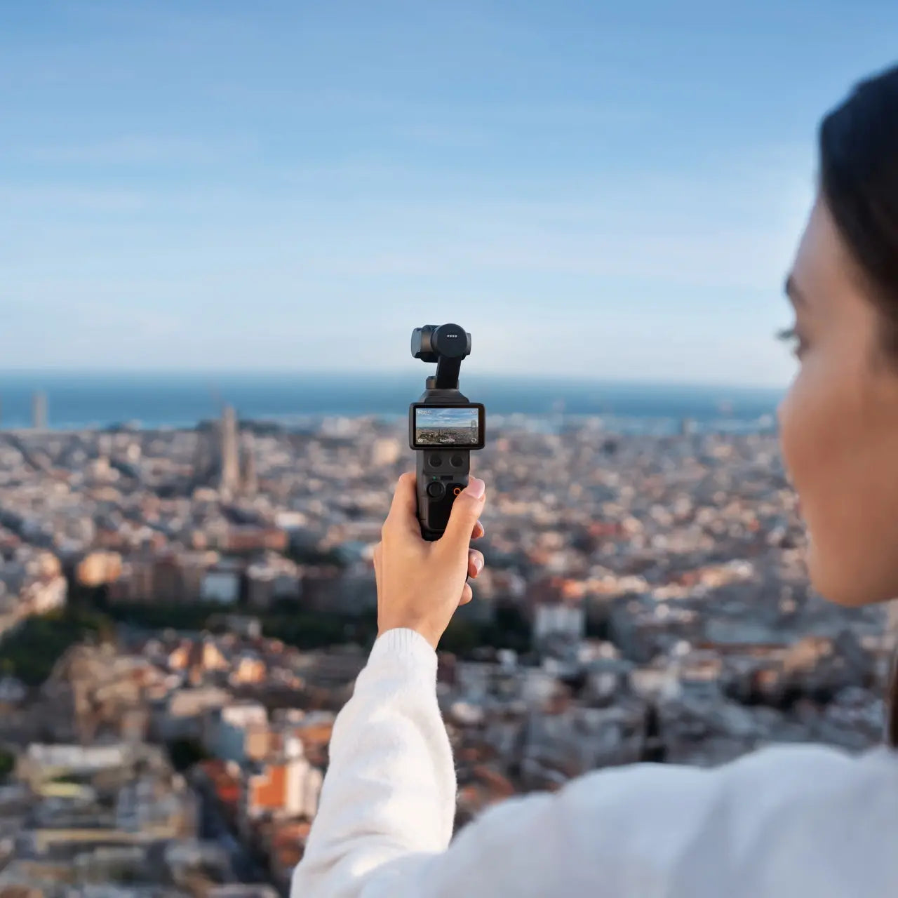 Person holding a camera over a cityscape with a clear blue sky